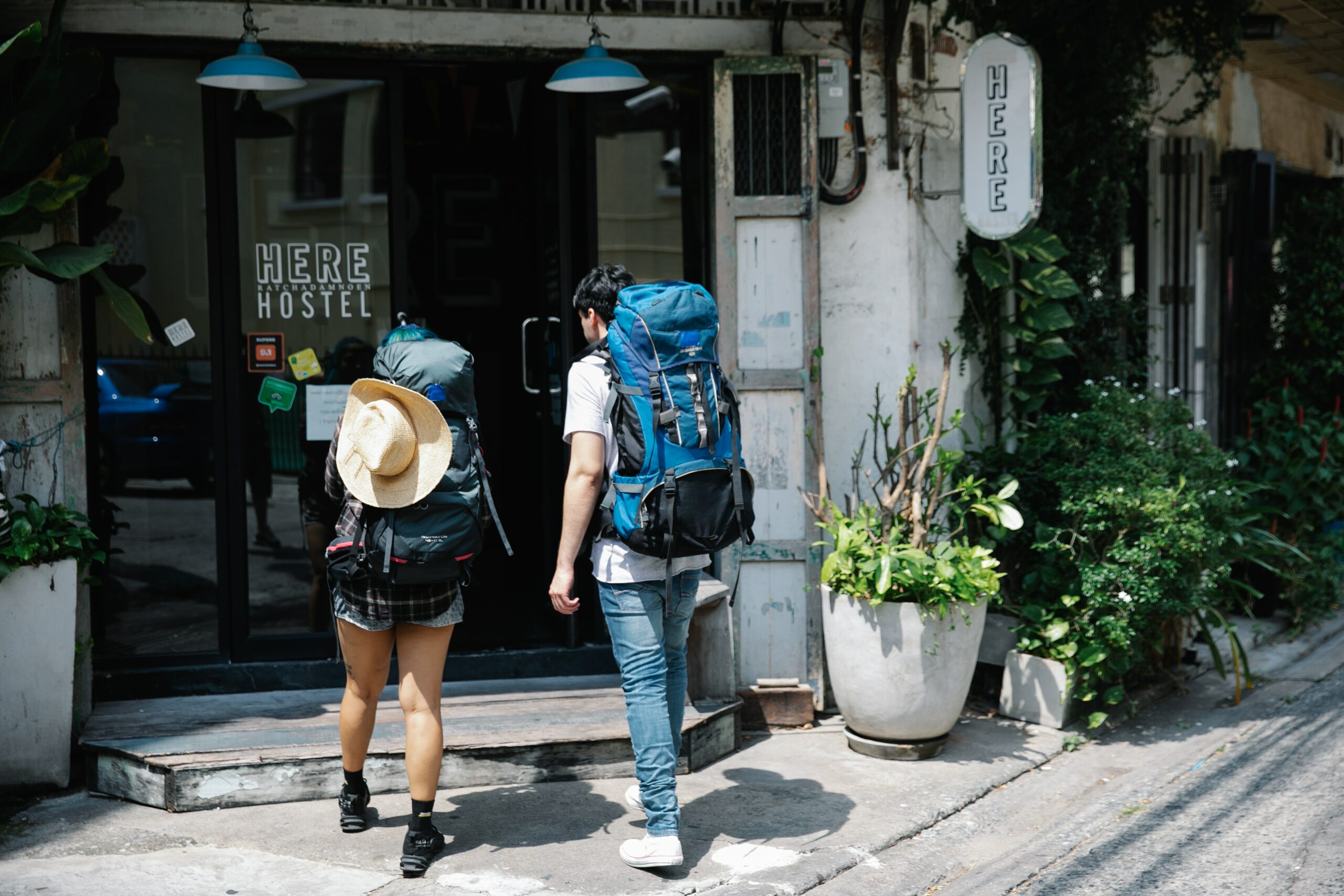 Un homme avec un grand sac à dos et une femme avec un grand sac à dos et un chapeau de paille marchent vers un hôtel, ils s'apprêtent à rentrer dedans